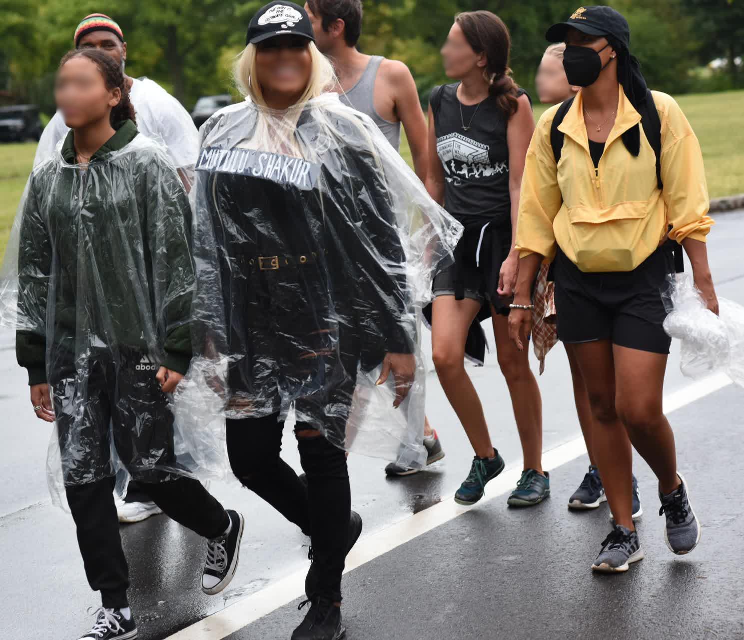 Group of seven people walking, some in rain jackets or ponchos, and others wearing just t-shirts and shorts.