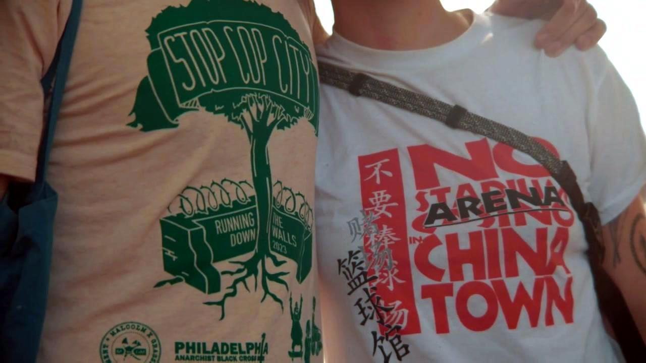 Close-up of someone wearing the RDTW 2023 shirt, standing next to someone wearing a No Arena in China Town shirt.